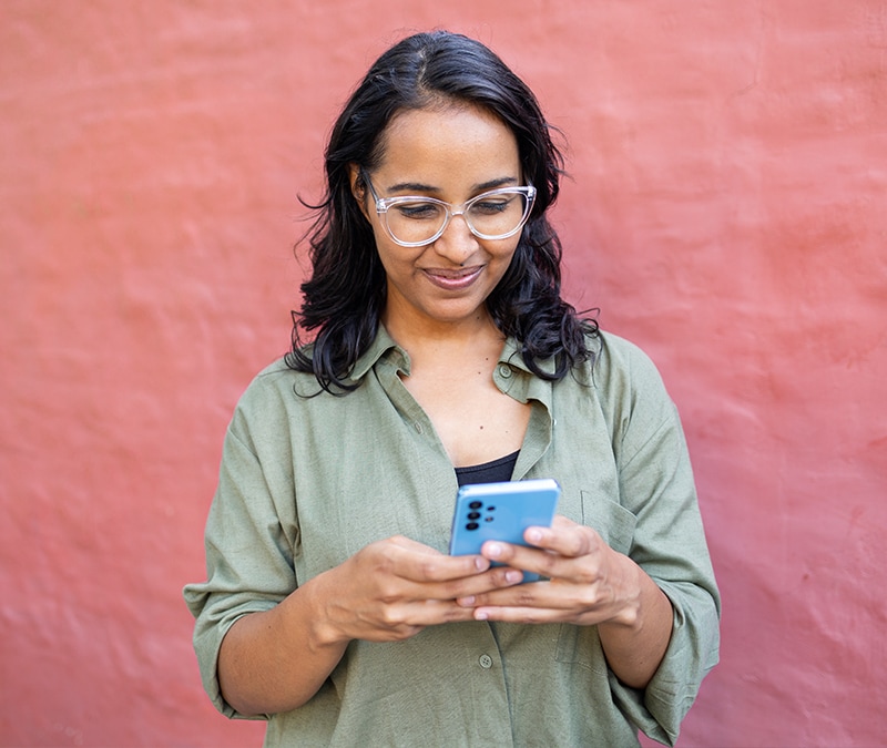 A woman wearing glasses focusedly looks at her phone screen.