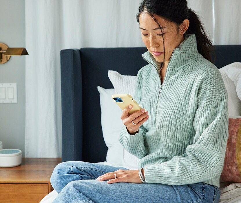 Woman sitting on the side of her bed looking at her phone.