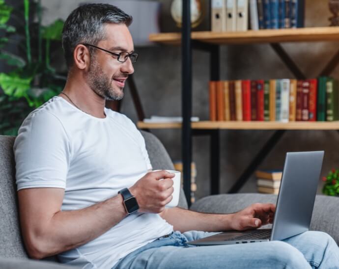 Man sitting down holding cup while using his laptop